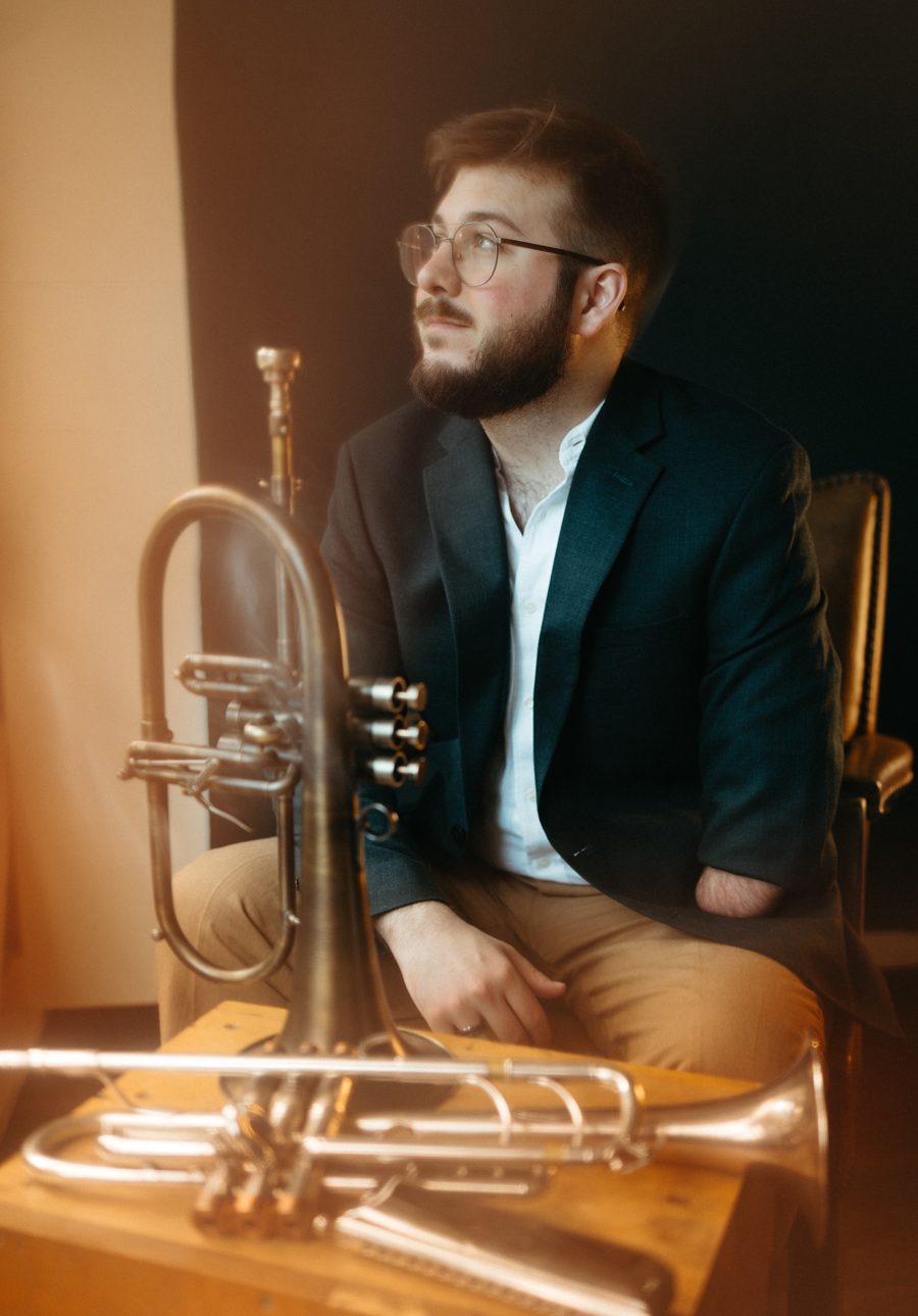 Christian Dyble seated in warm light beside his flugelhorn and trumpet, looking off to the side
