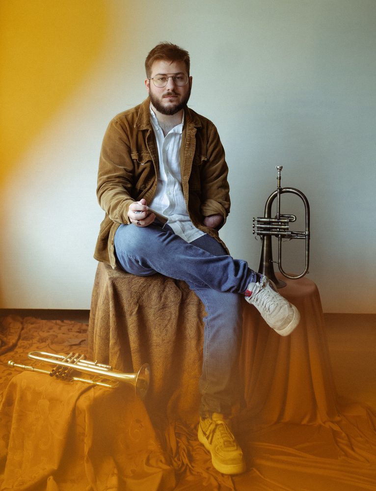 Christian seated on draped fabric with a flugelhorn and trumpet, golden light