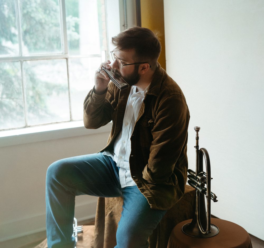 Christian playing harmonica by a window, flugelhorn beside him