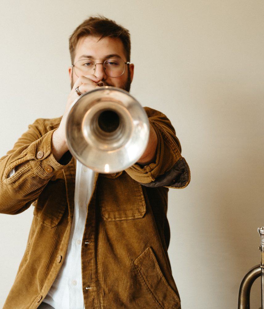 Christian playing trumpet straight toward the camera, bell in focus