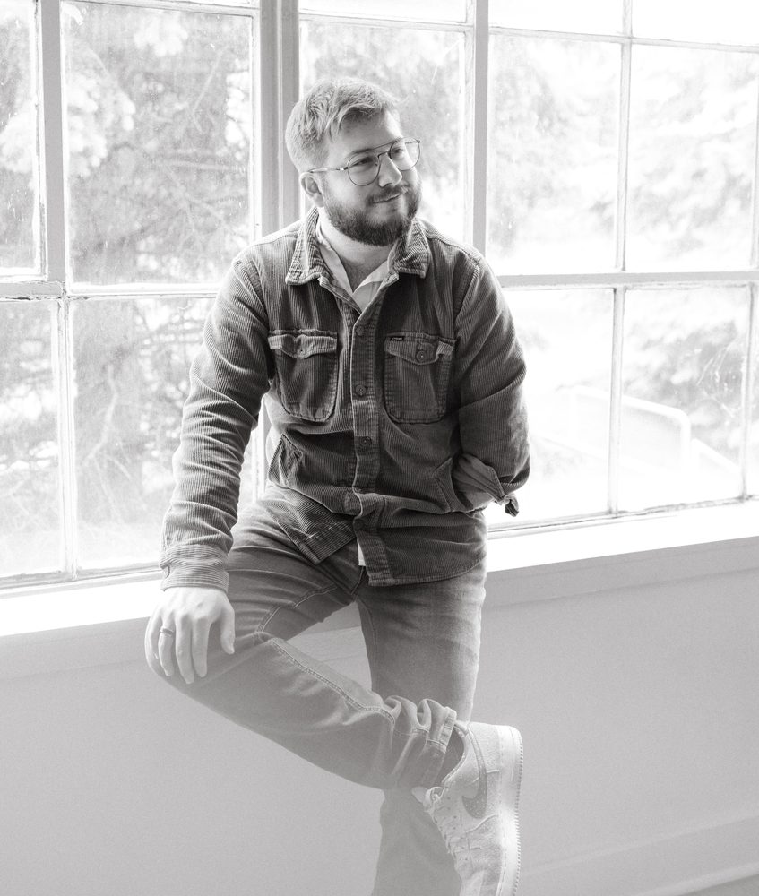 Black and white photo of Christian perched on a windowsill, smiling