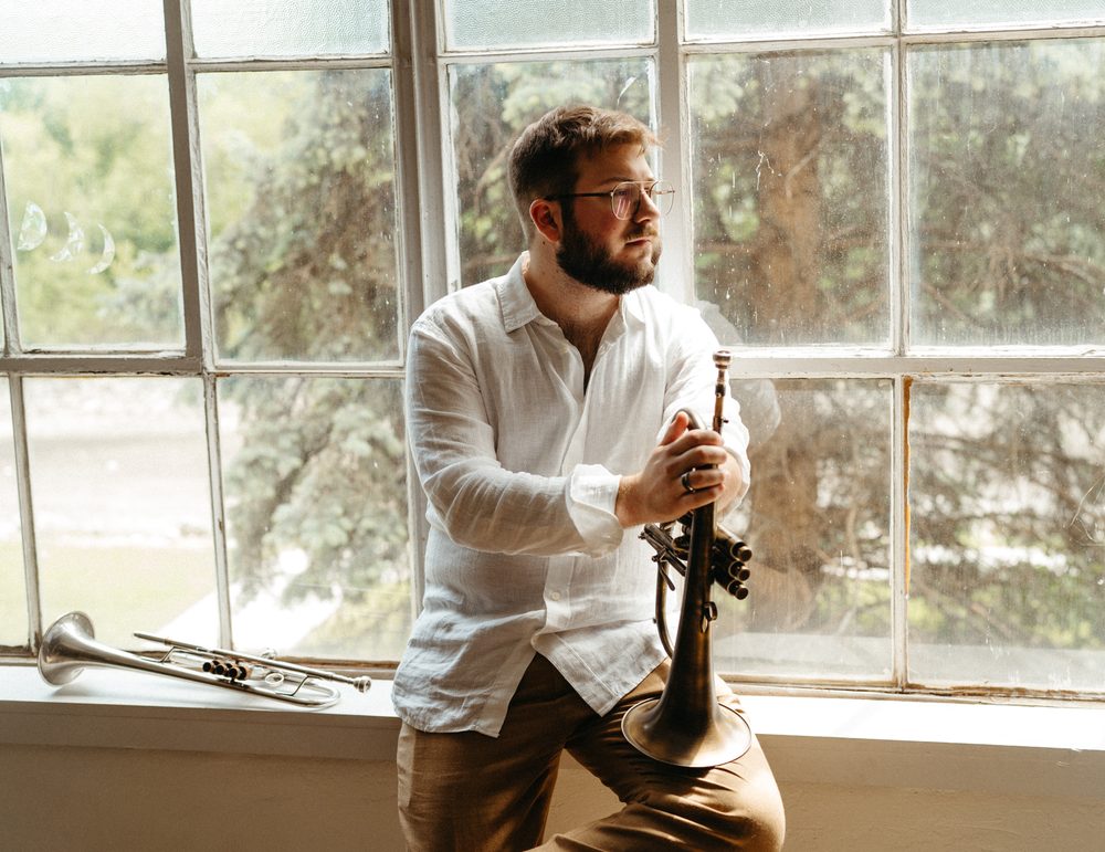 Christian in a white linen shirt leaning on a flugelhorn by the window