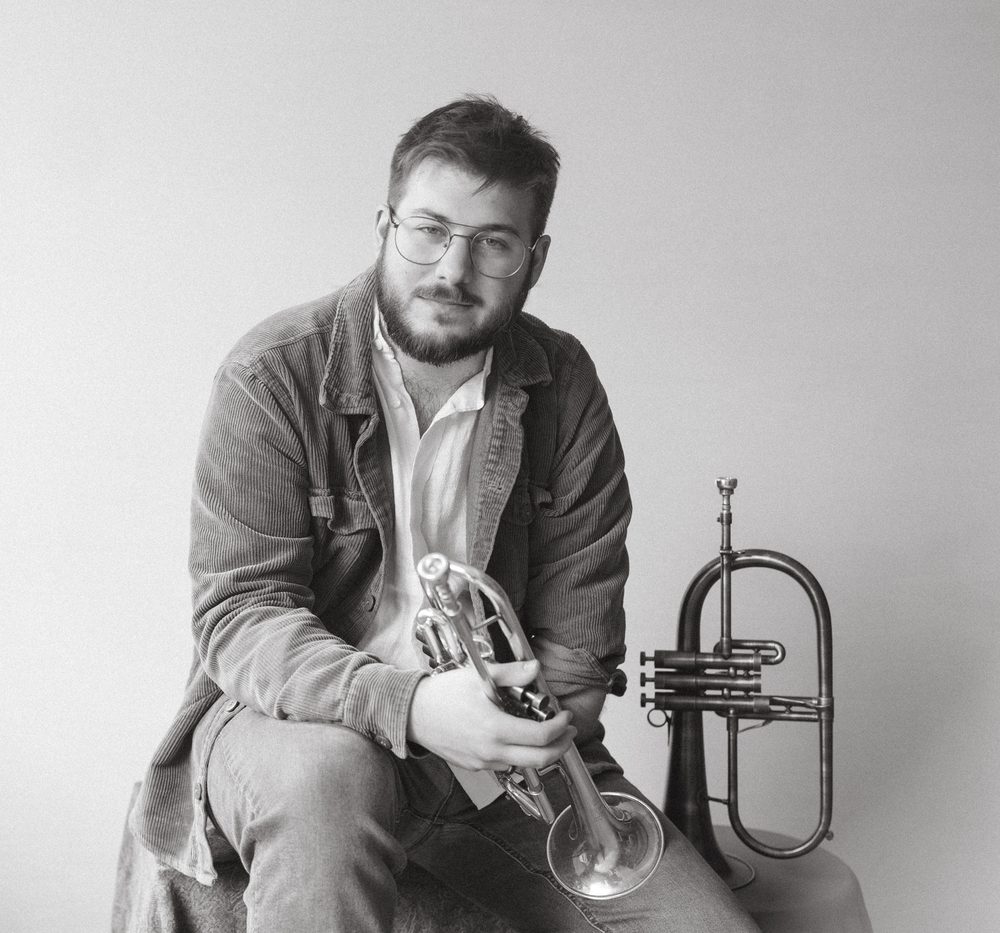 Black and white portrait of Christian holding a trumpet, flugelhorn standing beside him