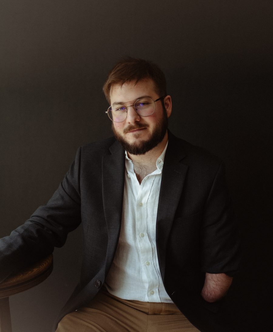 Portrait of Christian Dyble in a dark blazer and white shirt, seated against a dark backdrop